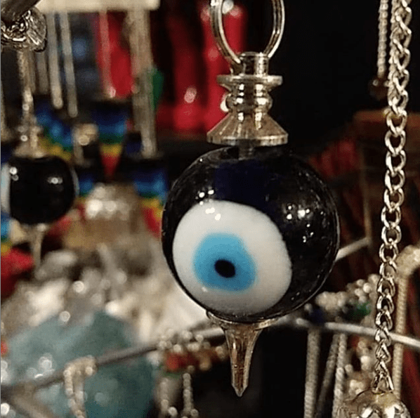 "Evil eye" pendulum with more pendulums and other merchandise on display in the background. This is both a product and the shop that sells it.